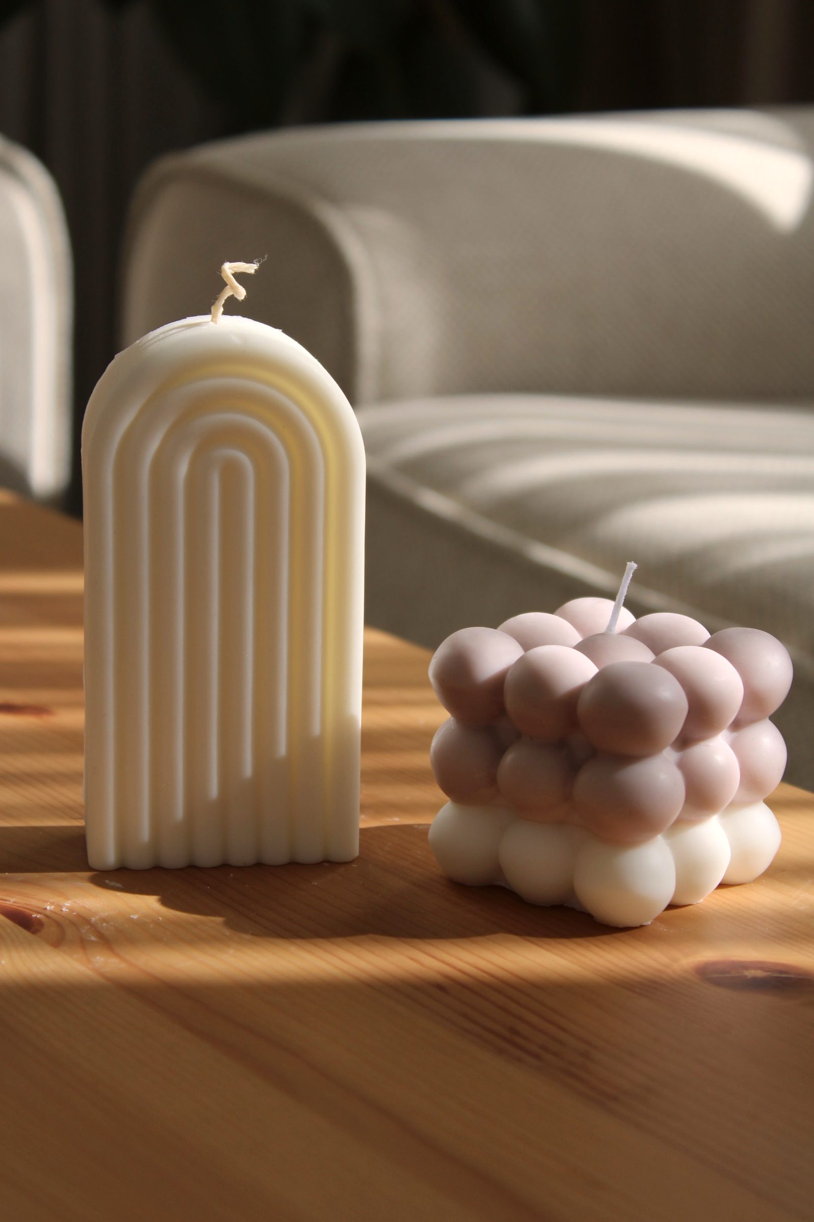 Modern candles with unique designs placed on a wooden table in a cozy room.