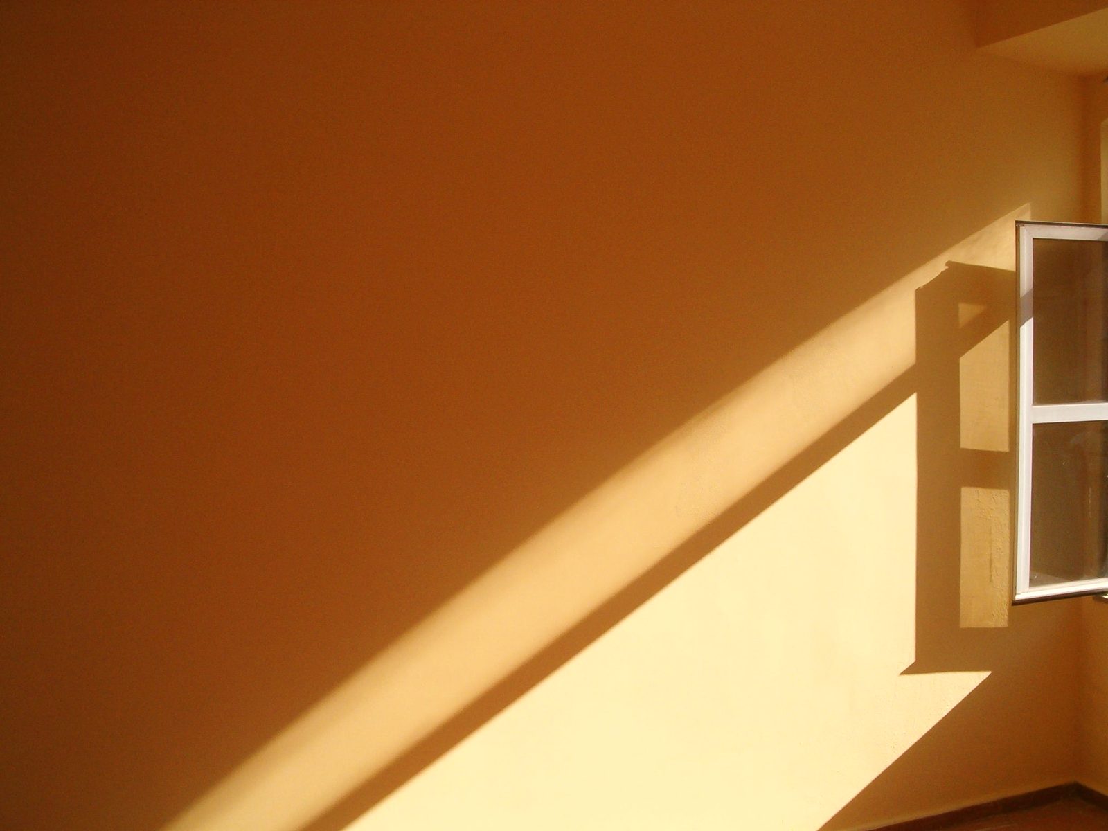 Warm sunlight streams through an open window, creating bold shadows on a yellow wall, offering a minimalist composition.